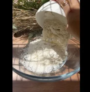 Pouring flour into a glass bowl for baking under natural sunlight.