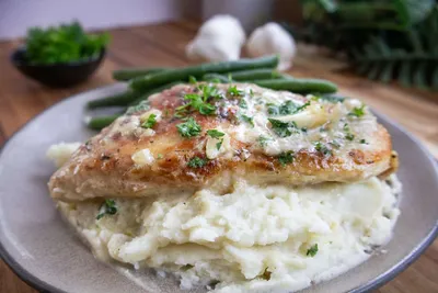 Creamy garlic chicken with mashed potatoes and green beans on a plate, garnished with fresh parsley.