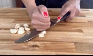 Crushing garlic cloves with a knife on a wooden cutting board.