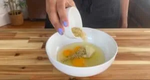 Mixing eggs, herbs, and cheese in a bowl on a wooden kitchen counter.