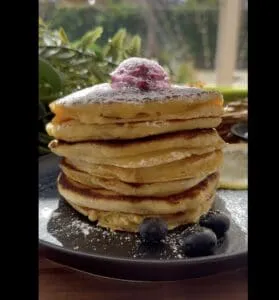 Stack of fluffy pancakes topped with berry cream and powdered sugar, served with fresh blueberries.