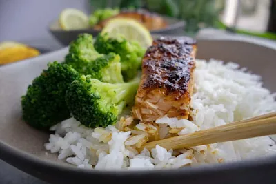Grilled honey orange salmon with broccoli and rice, garnished with lemon, in a ceramic bowl, close-up.