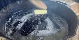 Melting butter in a cast iron skillet for cooking, creating bubbly texture.