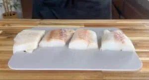 Four fresh fish fillets on a cutting board in the kitchen, ready for cooking.
