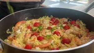 Pan of shrimp orzo with cherry tomatoes and herbs, garnished with parsley for a vibrant, flavorful dish.