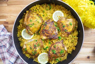 Savory lemon chicken with spiced rice in a pan, garnished with fresh herbs. Perfect for a flavorful dinner.