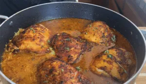 Spicy roasted chicken thighs in a pan with sauce and herbs, perfect for a flavorful dinner.