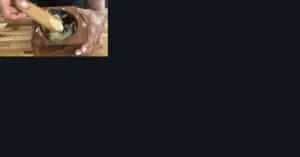 Crushing garlic in a wooden mortar and pestle on a wooden table for cooking.