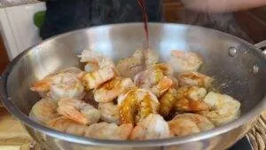Cooking shrimp in a pan with sauce being poured over, highlighting a savory seafood dish preparation.