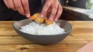 Placing succulent shrimp on a bowl of fluffy white rice, perfect for a delicious seafood meal preparation.