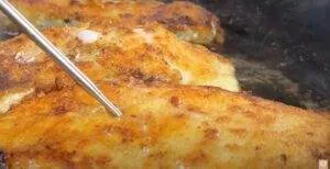 Golden-brown fish fillets being cooked in a pan with a probe thermometer nearby for temperature check.