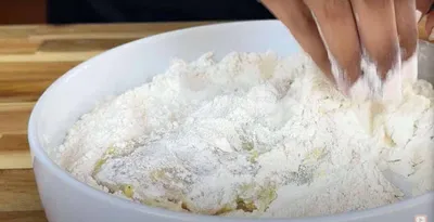 Hand mixing flour in a white bowl for baking preparation on a wooden surface.