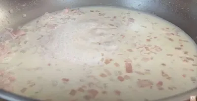 Creamy sauce with diced onions and ham simmering in a pan.