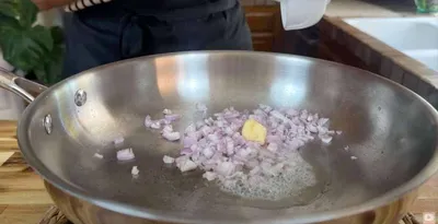 Cooking chopped onions and garlic in a stainless steel pan for a flavorful dish.