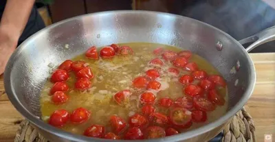 Cherry tomatoes simmering in olive oil and garlic in a skillet on a wooden surface.
