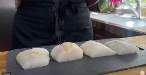 Chef seasoning cod fillets on a black cutting board in a kitchen setting.