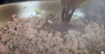 Ground beef and green onions sizzle in a pan as dark sauce is poured in, creating a flavorful meal.