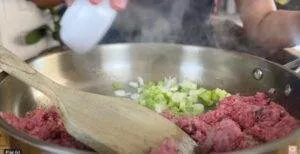 Cooking ground beef and fresh green onions in a skillet with a wooden spatula.