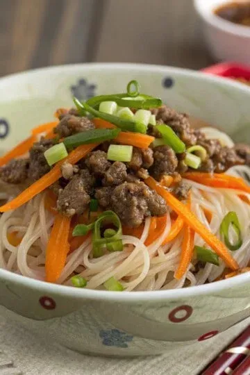 Bowl of Asian noodles topped with ground meat, carrots, and green onions for a flavorful dish.