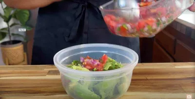 Person making fresh guacamole with avocado, tomato, and onion in a kitchen setting.