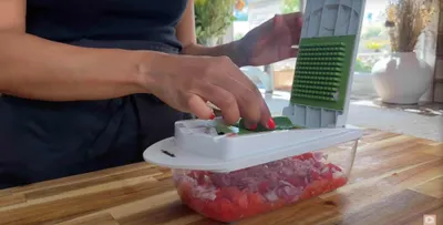 Person using a vegetable chopper to dice onions and tomatoes on a wooden countertop.