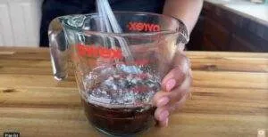 Person mixing ingredients in a Pyrex measuring cup on a wooden countertop.