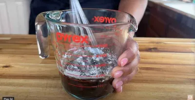 Person mixing ingredients in a Pyrex measuring cup on a wooden countertop.