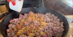 Seasoning ground beef in a cast iron skillet for cooking.
