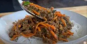 Bowl of Asian-style noodles topped with savory minced meat and julienned carrots, being served with a spoon.