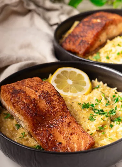 Lemon Garlic Salmon Orzo in a black bowl garnished with fresh herbs.