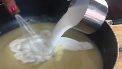 Pouring cream into saucepan, mixing ingredients for homemade sauce preparation.
