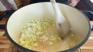 Cooking diced onions in a large pot with a wooden spoon, perfect for soups or stews.