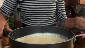 Person stirring creamy sauce in a pot in a cozy kitchen setting.