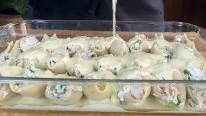 Cheesy stuffed pasta shells in a glass dish, covered with creamy sauce, ready for baking. Perfect Italian comfort food.
