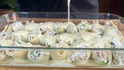 Cheesy stuffed pasta shells in a glass dish, covered with creamy sauce, ready for baking. Perfect Italian comfort food.