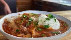 Bowl of delicious lasagna soup topped with ricotta and fresh parsley, served on a wooden table.