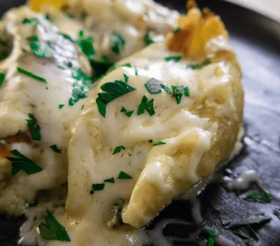 Chicken alfredo stuffed shells topped with fresh parsley on a black plate.