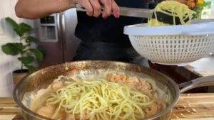 Cooking shrimp pasta with creamy sauce in a kitchen; spaghetti being added to sauce.