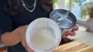 Person holding open blender cup with white smoothie inside in a kitchen setting.