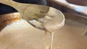 Wooden spoon with creamy spiced sauce dripping into a pot, perfect for cooking a flavorful dish.