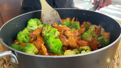 Cooking delicious chicken and broccoli stir-fry in a pan with wooden spatula. Healthy dinner preparation.