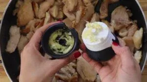 Minced garlic in a grinder above cooked chicken in a pan, ready for cooking enhancement.