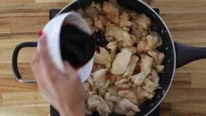 Pouring sauce over cooked chicken pieces in a frying pan for a savory meal preparation.