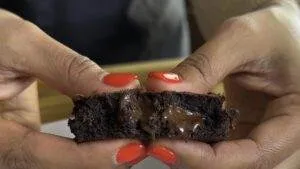 Close-up of hands pulling apart a gooey chocolate cookie with vibrant red nails.