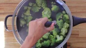Broccoli in a steaming pot on a wooden kitchen countertop. Healthy cooking preparation.