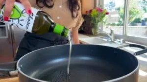 Pouring avocado oil into a pan in a bright kitchen setting. Healthy cooking preparation.
