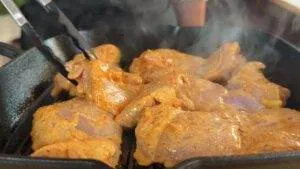 Marinated chicken thighs sizzling on a grill pan with steam rising, held with tongs for a delicious meal.