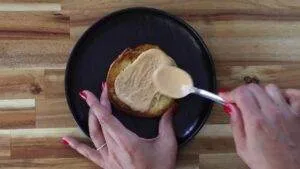 Woman spreading peanut butter on toast with a spoon on a black plate.