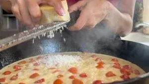 Grating cheese over a sauce in a black skillet, steam rising from the pan.