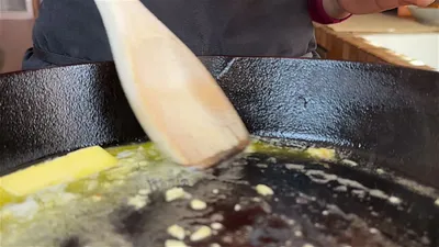Melting butter in a cast iron skillet with a wooden spatula stirring in garlic.